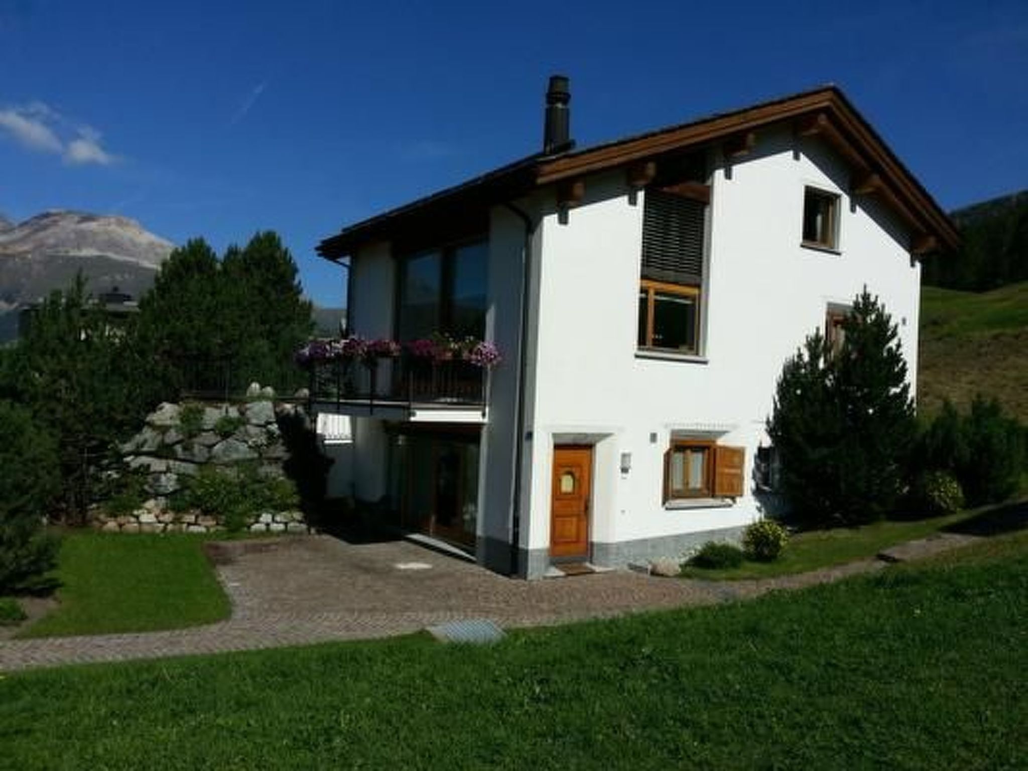 Een woonhuis met twee verdiepingen, een balkon, een stenen muur en een berg op de achtergrond.