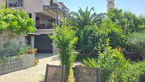 Un edificio residencial con balcón, un jardín con diversas plantas y una estructura en forma de torre al fondo.