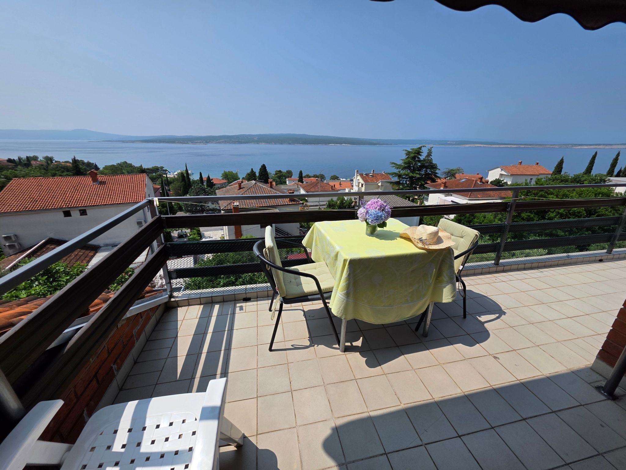 A balcony with a table and chairs, overlooking a body of water and distant hills.
