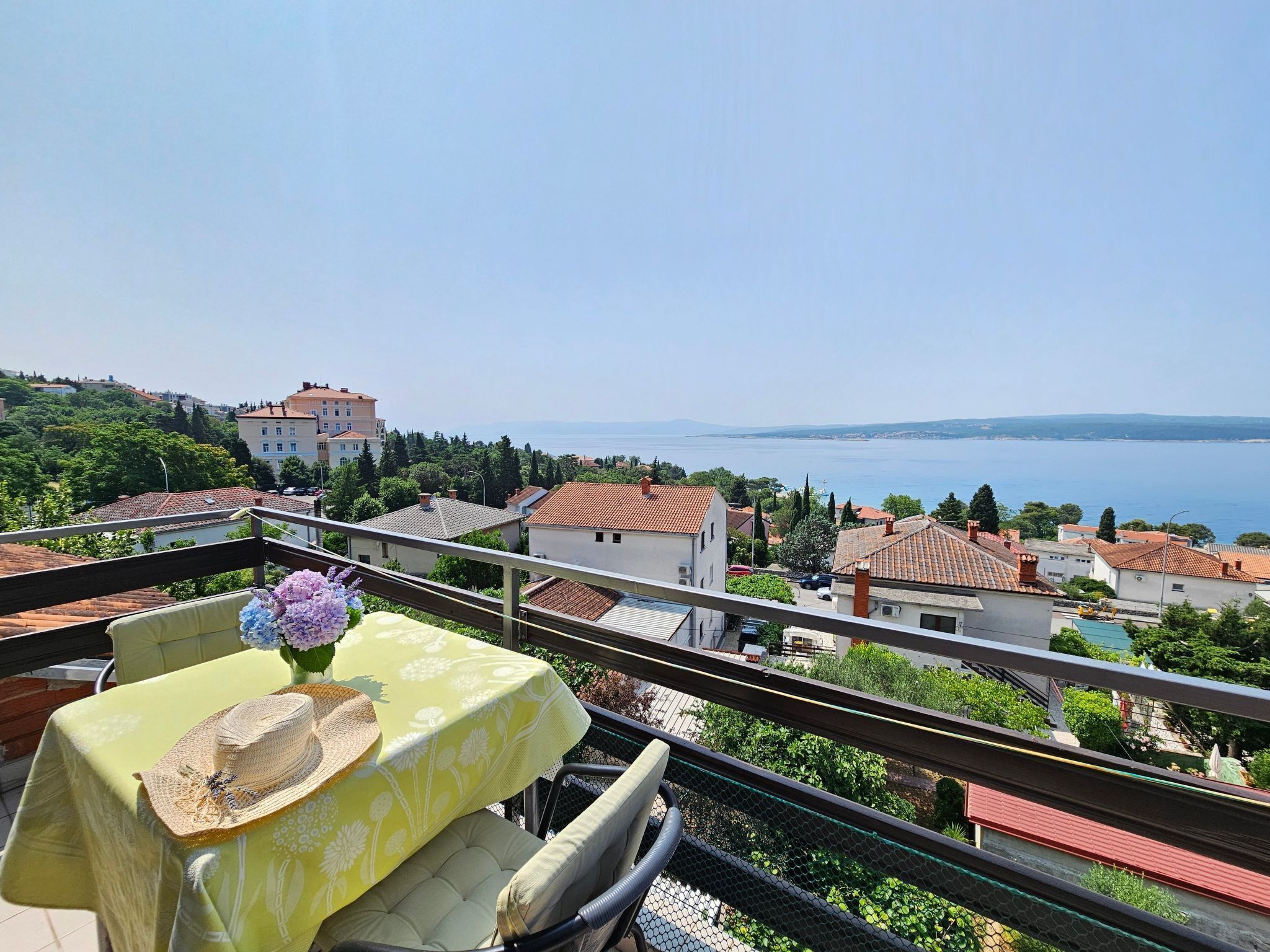 Un balcone con tavolo apparecchiato per due, vista su una località costiera con edifici e il mare.