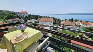 Ein Balkon mit Tisch für zwei Personen, mit Blick auf eine Küstenstadt, Gebäude und eine Meeransicht.