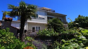 Ein zweistöckiges Haus mit Balkon, umgeben von üppiger Vegetation und blauem Himmel.