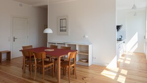 Tilava ruokailutila, jossa on puinen pöytä ja tuolit, valkoinen riippuvalaisin sekä valkoinen kaappi, jossa säilytetään keittiötarvikkeita.