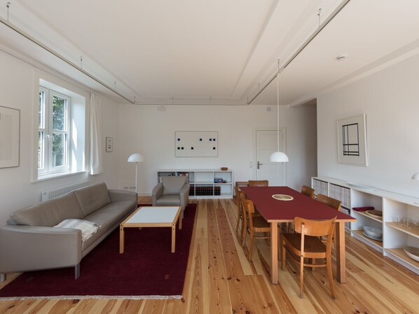 Una sala de estar moderna con un sofá, una mesa de centro, una mesa de comedor con sillas, una estantería y un radiador.
