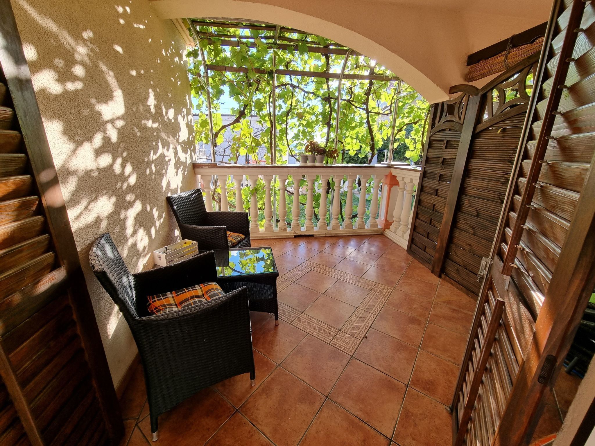 A balcony with wicker furniture, a tiled floor, and a view of greenery.