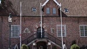 En byggnad av tegel med ett tak täckt av takpannor, en central entré med en trappa och krukväxter framför.