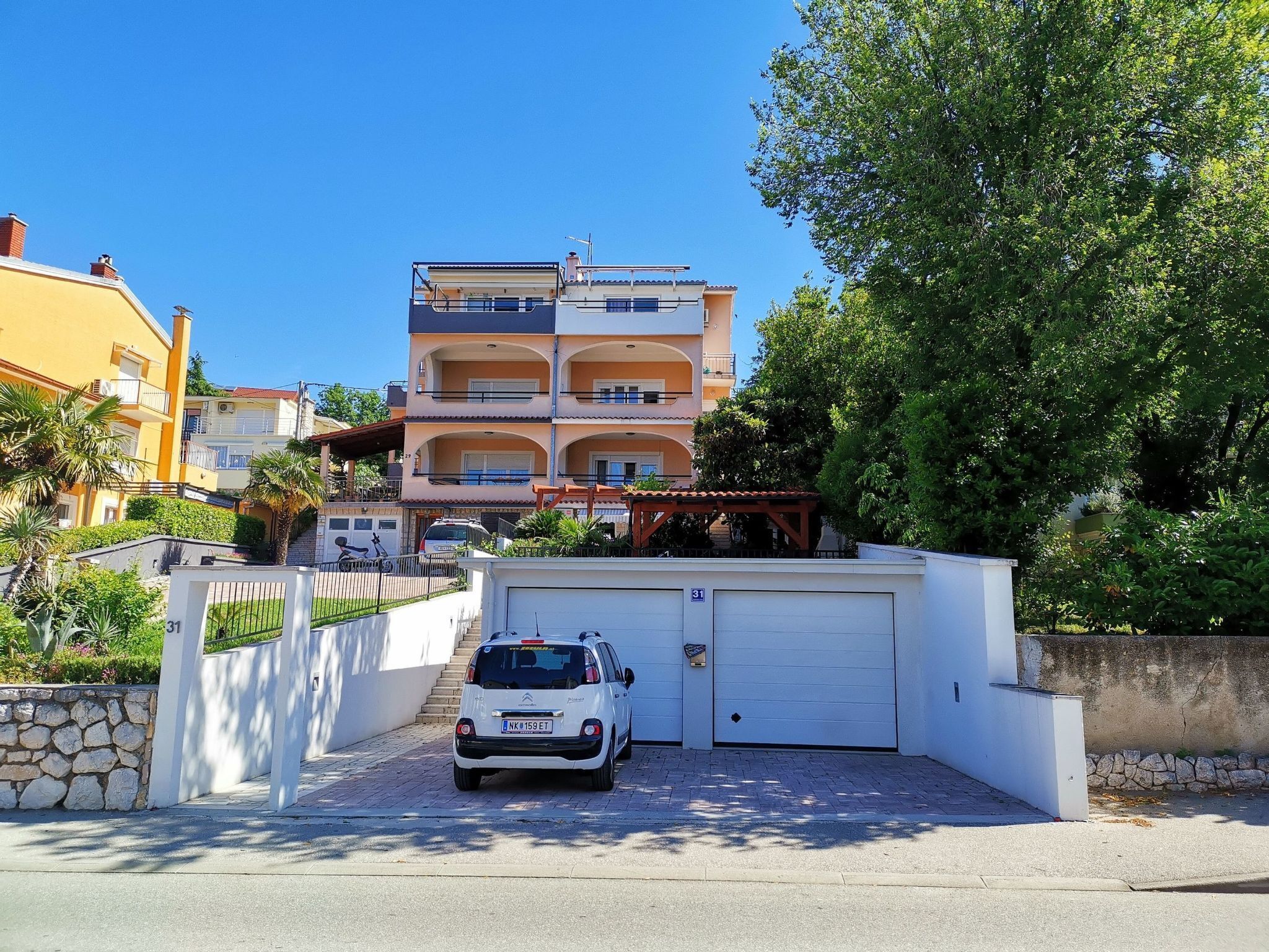 A multi-story residential building with a white garage door, a parked car, and a stone wall.