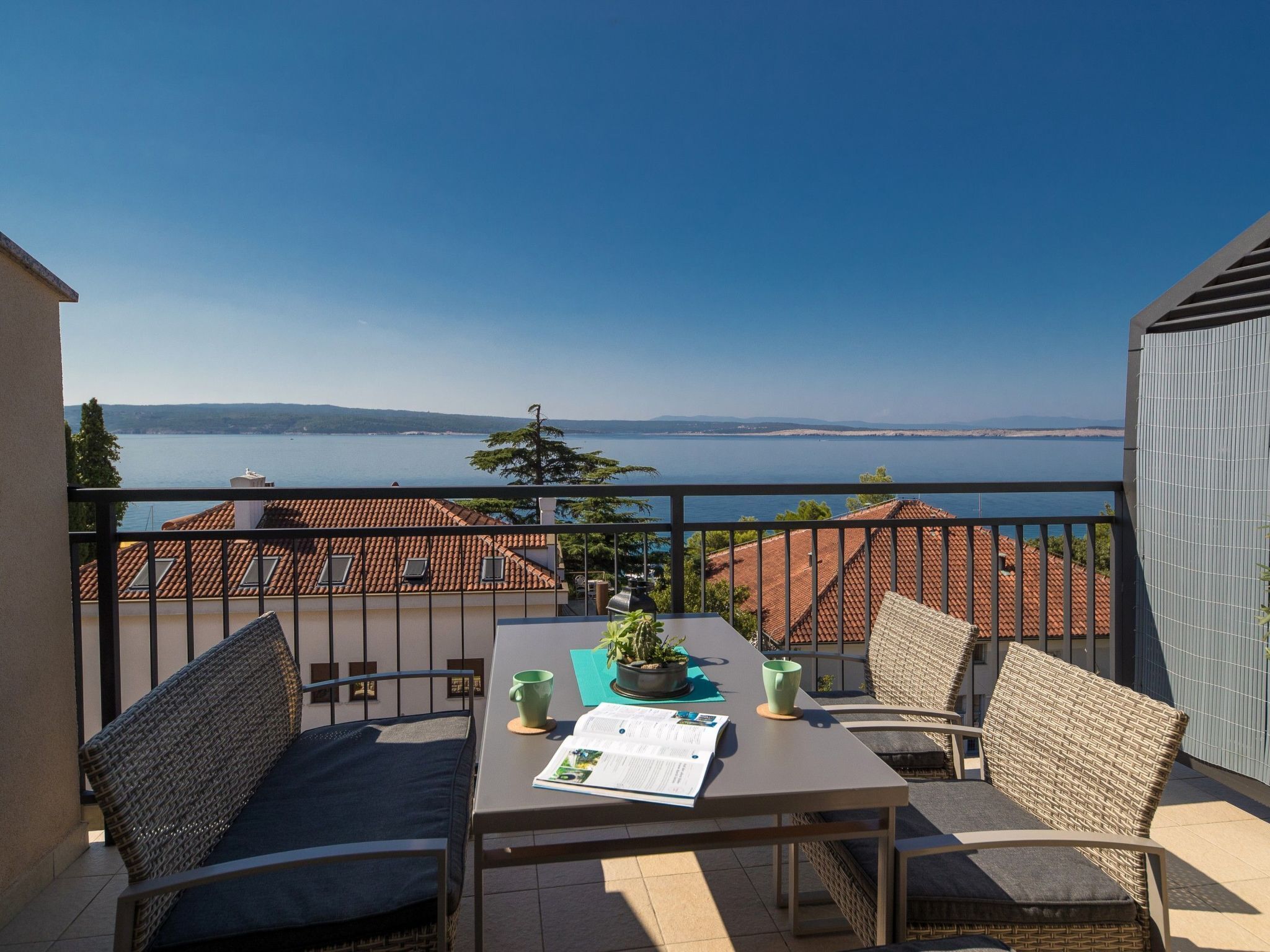A balcony with a table, chairs, and a view of the sea.