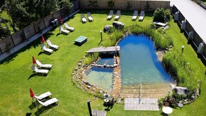 A backyard with a small pond, several lounge chairs, a swing set, and a patio table. - Bio-Haus # 401 by Interhome (Neukirchen am Großvenediger)
