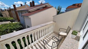 Ein Balkon mit weißer Brüstung, einem einzelnen Stuhl und einem kleinen Topfpflanzen.