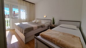 Ein Schlafzimmer mit Bett, Nachttisch, Vorhängen und Blick auf Gebäude.