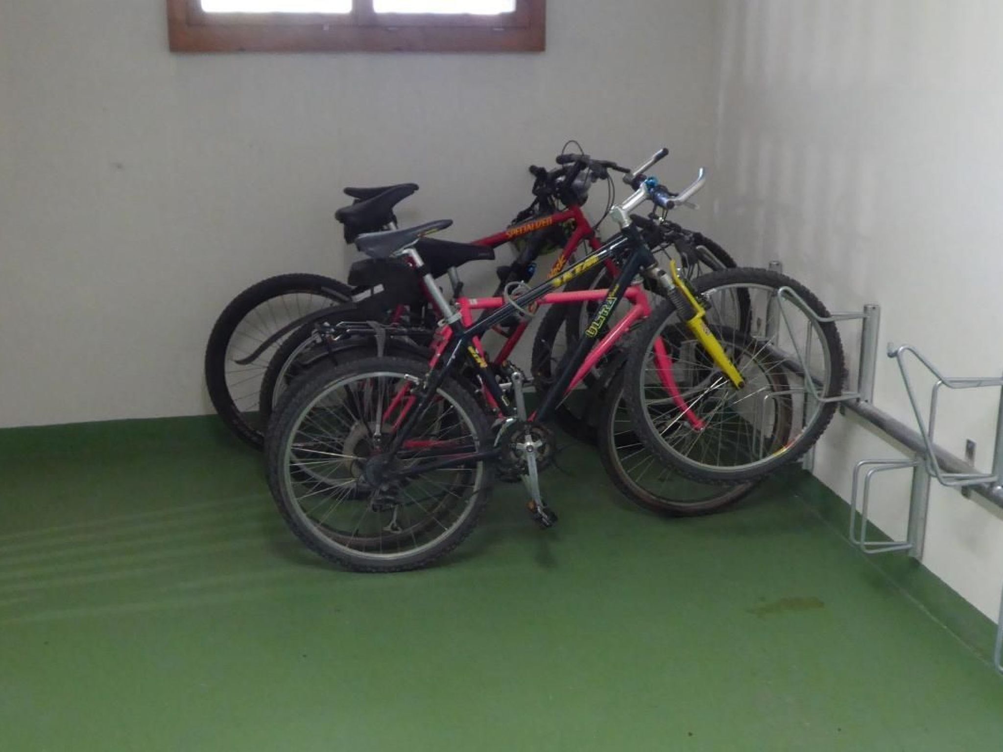 Ett rum med en grön matta, ett fönster och tre cyklar.