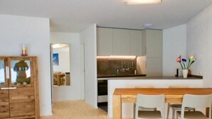 A modern kitchen with a central island, wooden cabinets, and a dining area with a table and chairs. - Chesa Auricula by Interhome (Pontresina)
