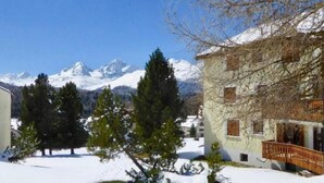 A snow-covered landscape with a building featuring a balcony and a view of snow-capped mountains. - Chesa Auricula by Interhome (Pontresina)