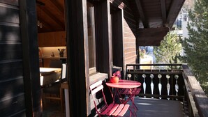 Una terraza de madera con una mesa y sillas rojas, vista a la ciudad y barandilla de balcón.