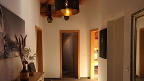 Un pasillo con un banco de madera, un jarrón con flores y un cuadro en la pared. Hay puertas que dan a otras habitaciones.
