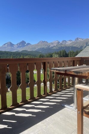 Un balcon doté d’une balustrade en bois et d’une table, offrant une vue sur un paysage montagneux.