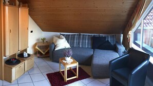 Una habitación acogedora estilo loft con techo inclinado, un sofá gris, un mueble de madera y una pequeña mesa con una planta.