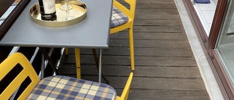Un patio al aire libre con sillas amarillas y una mesa, una botella de vino y una copa sobre la mesa.