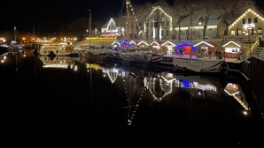 Una marina de noche con barcos amarrados, edificios iluminados y reflejos en el agua.