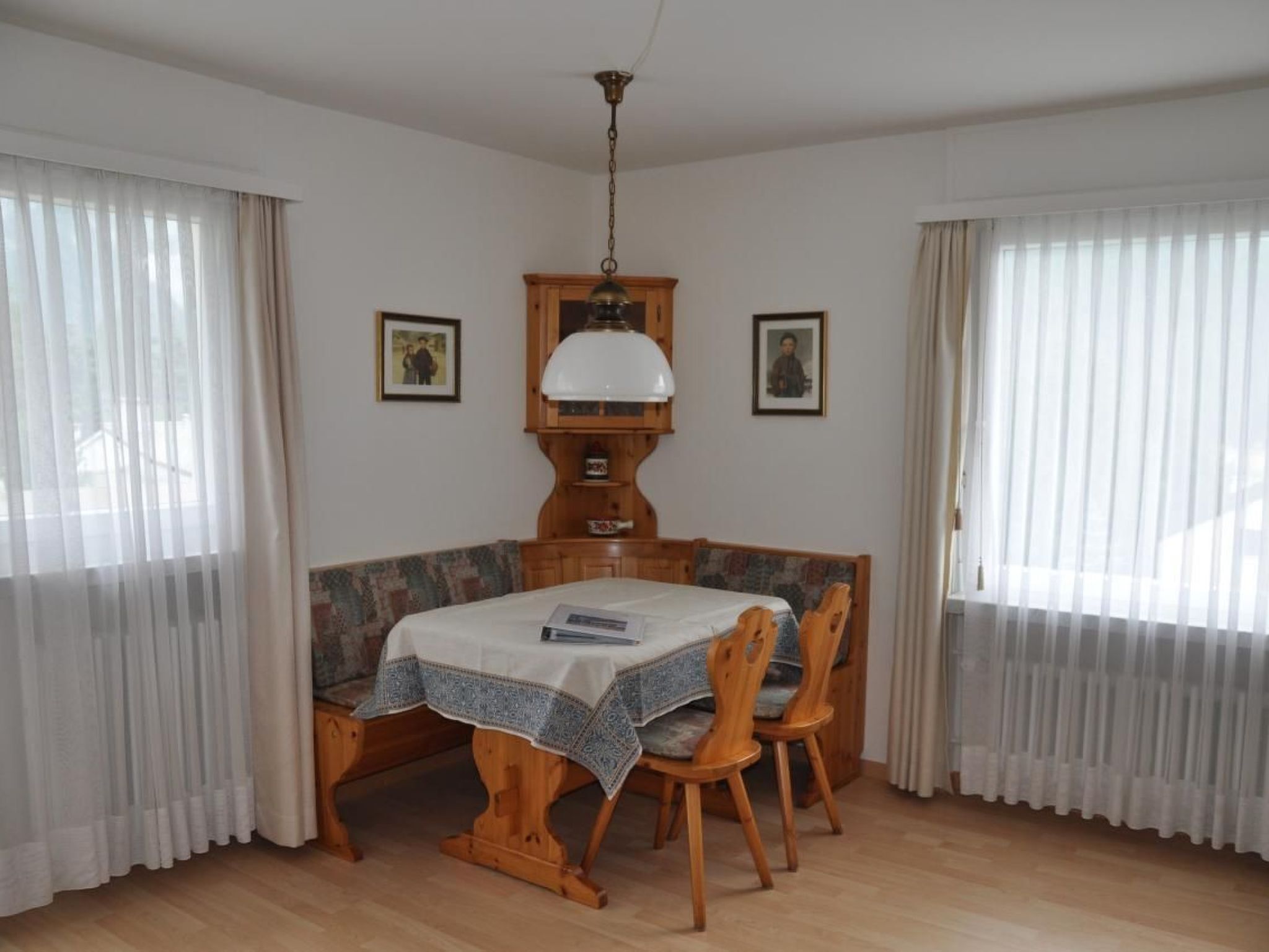 A dining room with a wooden table and chairs, a patterned bench, and two framed pictures on the walls.