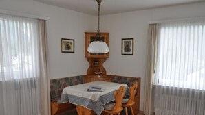 Ein Esszimmer mit Holztisch und -stühlen, einer gemusterten Bank und zwei gerahmten Bildern an den Wänden.