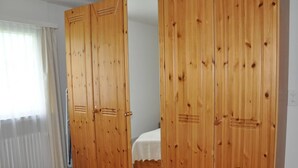 Ein Schlafzimmer mit Holzschrank, Bett und einem Fenster mit Vorhängen.