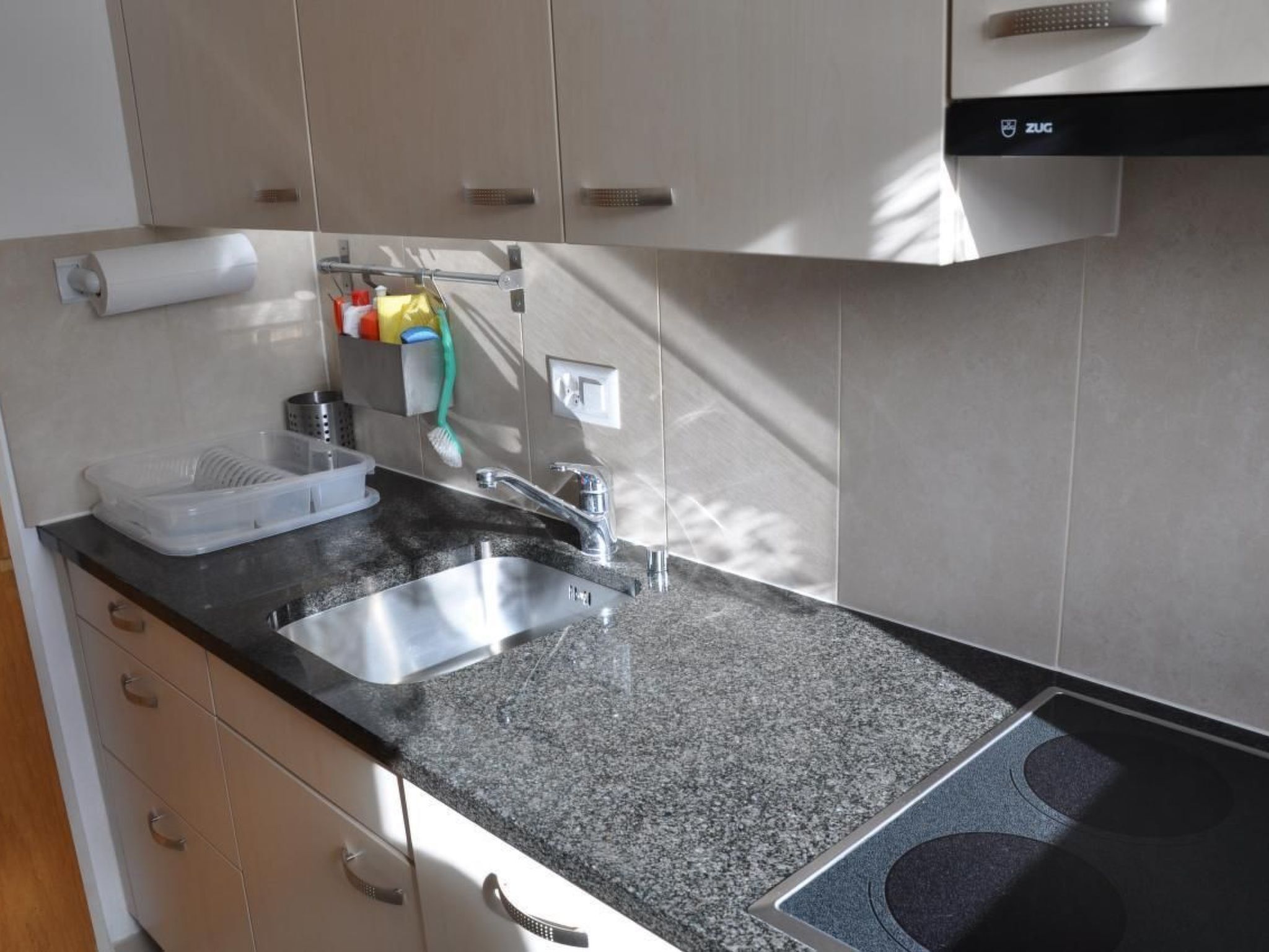 A kitchen with a granite countertop, stainless steel sink, and a ZUG dishwasher.