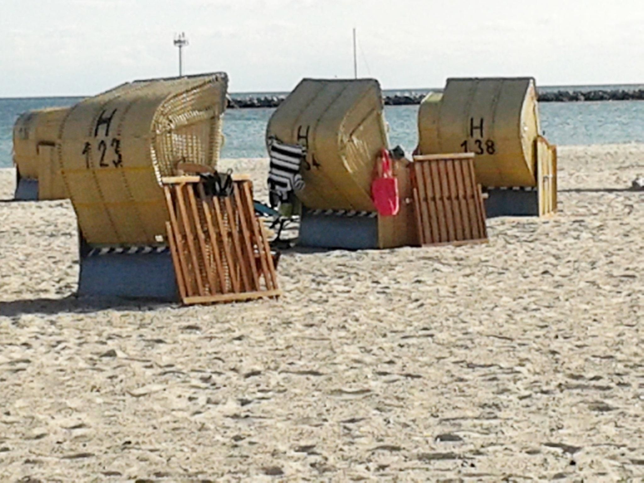 Three beach huts with numbers H 23, H 38, and H 13 on them, situated on a sandy beach with a calm sea in the background.