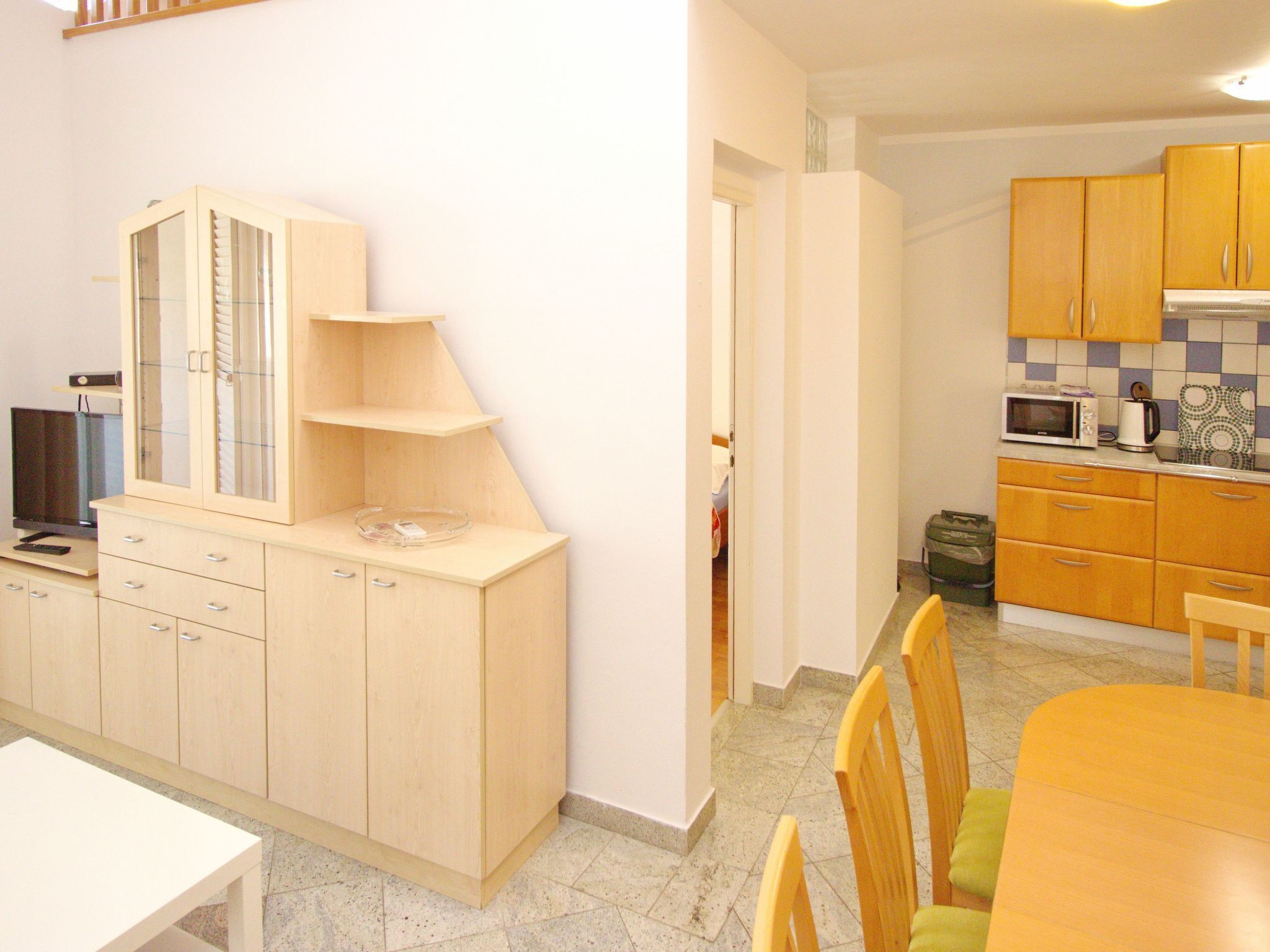 A compact kitchen with wooden cabinets, a microwave, and a small dining area with chairs.
