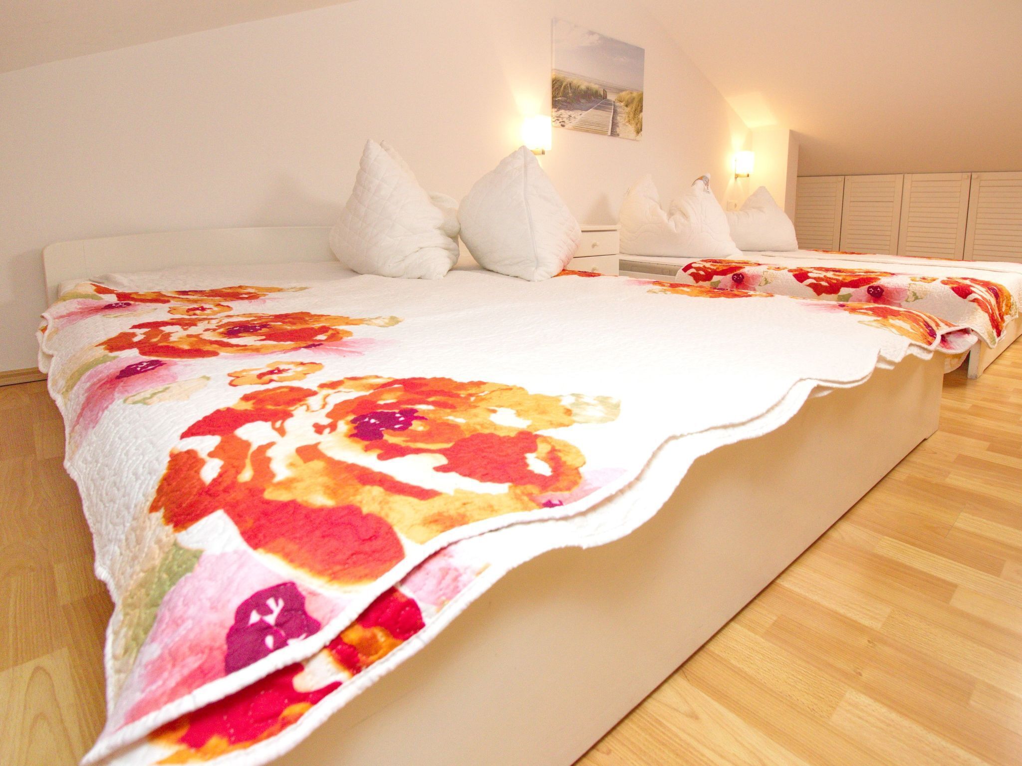 Een groot bed met een bloemenbedekking, twee witte kussens en een nachtkastje met een lamp.