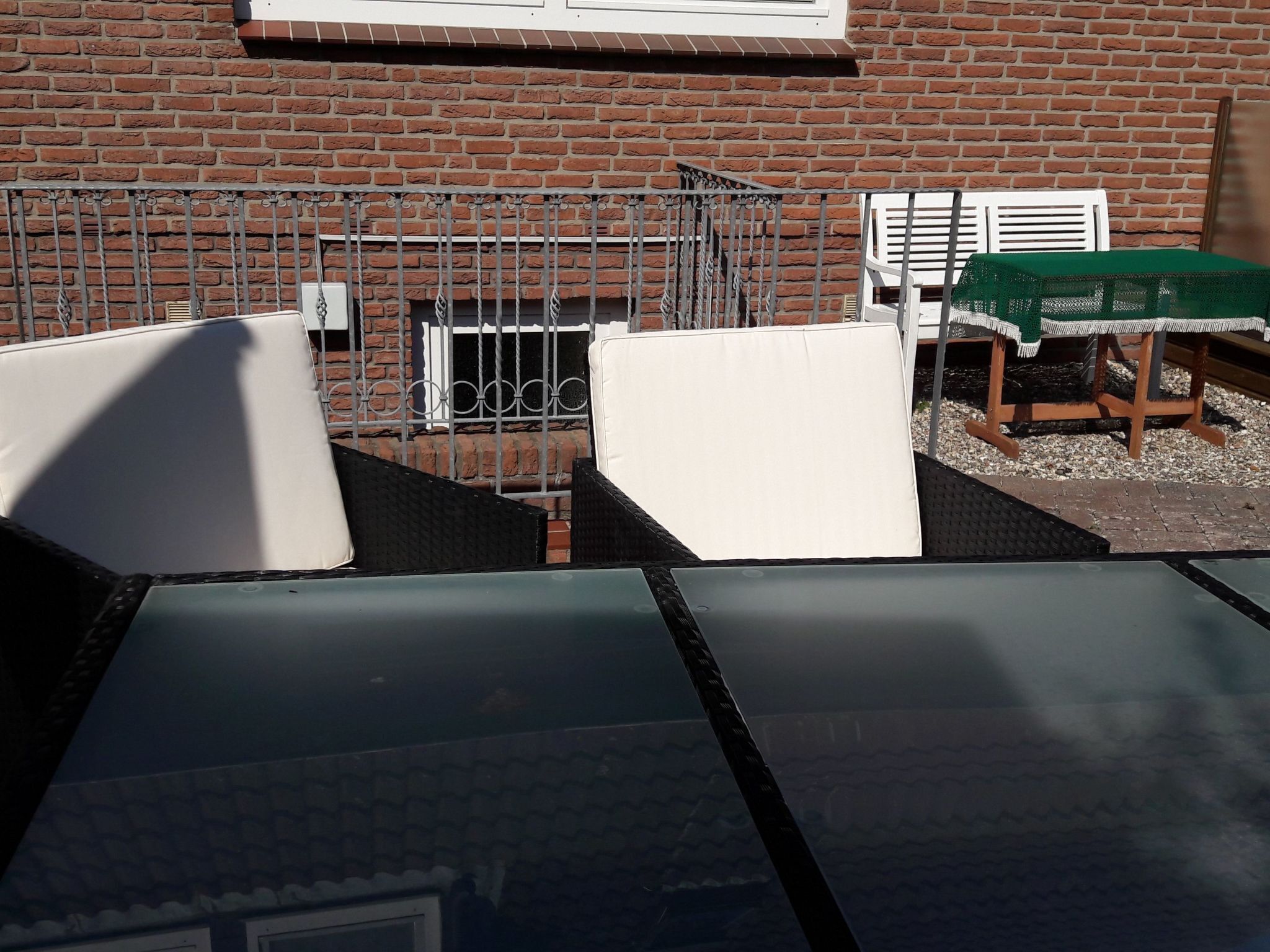 Eine Dachterrasse mit Backsteinmauer, Metallgeländer und einem Tisch mit grüner Tischdecke.
