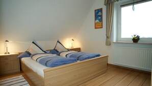 Ein Schlafzimmer mit einem hölzernen Bett, zwei Nachttischen, einem Fenster mit Vorhängen und einer Heizung.