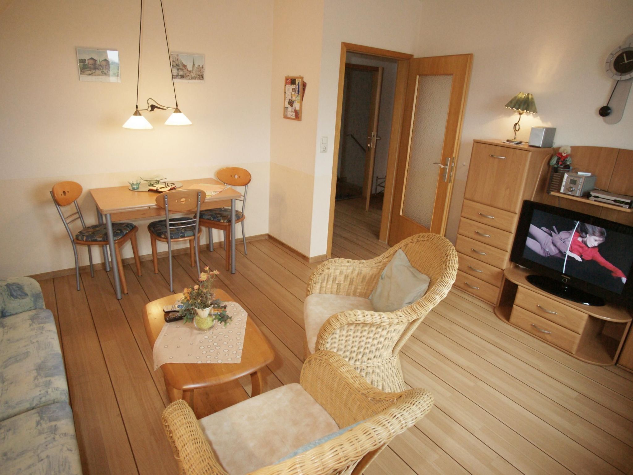 A cozy living room with a dining area, wicker furniture, a television, and wooden flooring.
