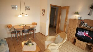 Ein gemütliches Wohnzimmer mit Essbereich, Korbmöbeln, einem Fernseher und Holzböden.