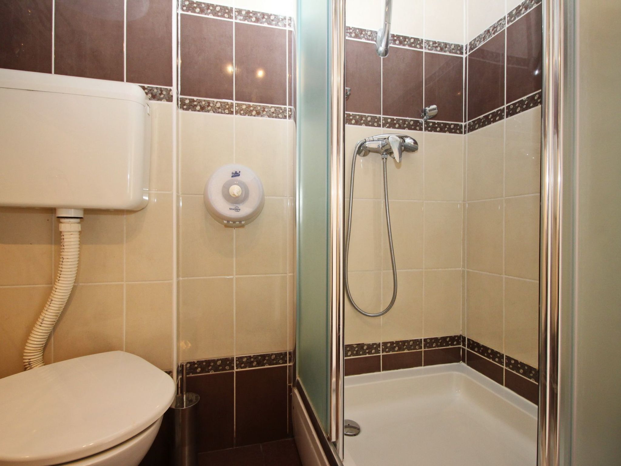 A bathroom with a toilet, a hand dryer, and a shower with a glass door.