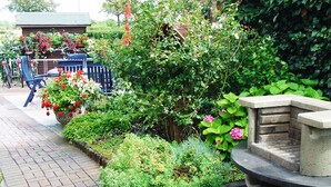 Ein Gartenpfad mit Ziegelsteinkanten, einer Steinsitzbank und verschiedenen Pflanzen und Blumen.