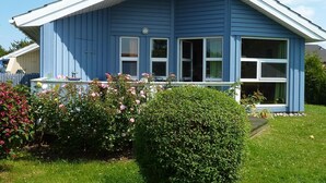 A two-story blue house with a white porch, large windows, and a small garden with pink flowers. - Dänemark in Gelting by Interhome (Gelting)
