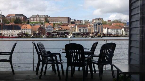 A deck with chairs overlooking a waterfront with buildings in the background. - Dänemark in Gelting by Interhome (Gelting)