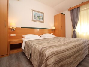 Habitación de hotel con cama, dos lámparas de noche, mesita de noche, armario de madera y un cuadro en la pared.
