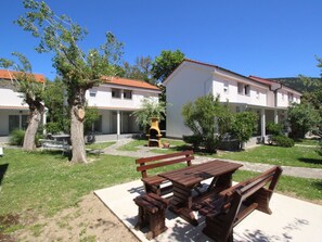 Un patio con banco de madera y mesa de picnic, rodeado de edificios blancos con tejados rojos.