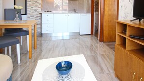 Una cucina moderna con mobili bianchi, una zona pranzo con tavolo e sedie, un televisore su un supporto in legno e una ciotola decorativa su un tappetino bianco.