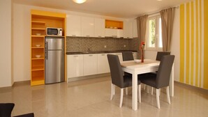 Una cucina moderna con mobili bianchi, un frigorifero in acciaio inossidabile e un forno a microonde. C'è un tavolo da pranzo con quattro sedie e un vaso con fiori.