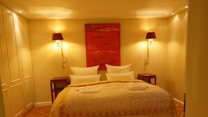 Une chambre d’hôtel avec un lit, deux lampes de chevet, une œuvre d’art rouge accrochée au mur et un banc au pied du lit.