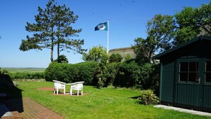 Un jardin bien entretenu avec deux chaises blanches, un mât avec un drapeau et un abri de jardin vert.