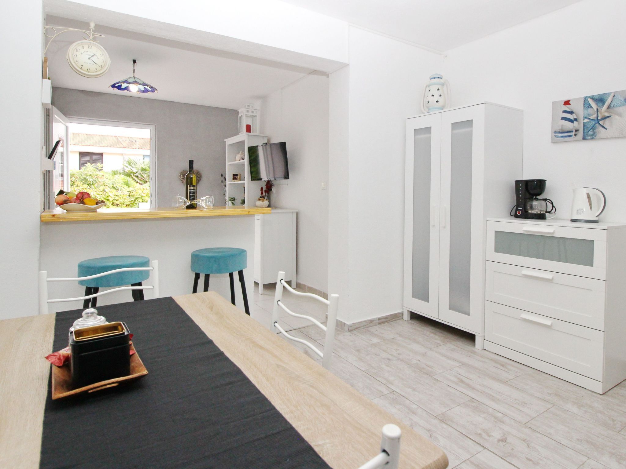 Una cocina moderna con comedor, armarios blancos, cafetera y televisor.