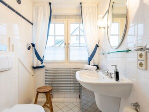 A bathroom with a white sink, a wooden stool, a towel rack, and a window with curtains. - Heefwai - H2W6 - in Morsum by Interhome (Archsum)