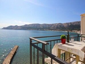 Varanda com vista desobstruída para um lago e montanhas, mesa com toalha, planta em vaso e uma garrafa.