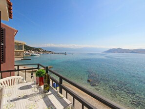 Varanda com mesa posta para refeições, com vista para o mar calmo, barcos e uma cadeia montanhosa ao longe.