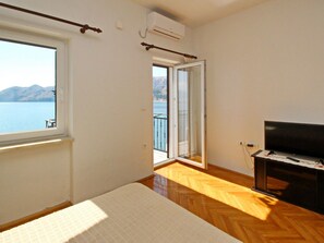 Quarto com cama, televisão e uma janela grande com vista para a água.